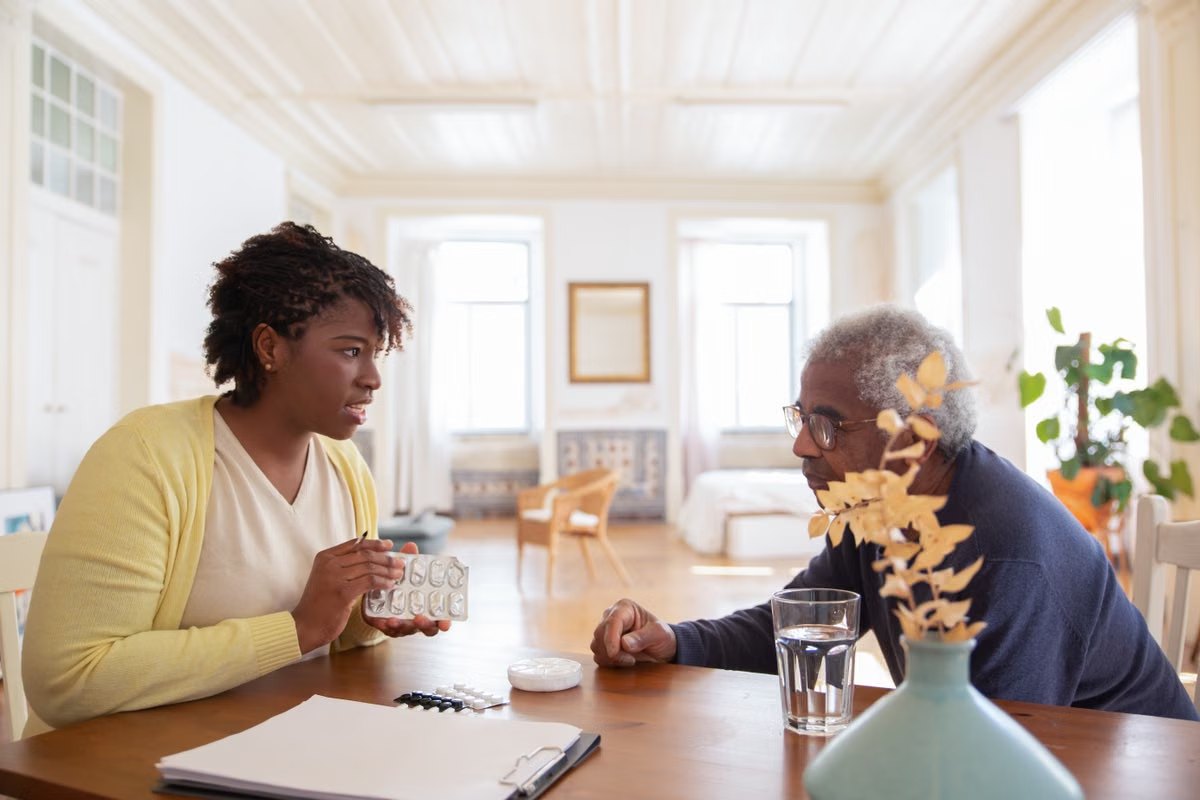 A caregiver going over medication with a senior man at his table