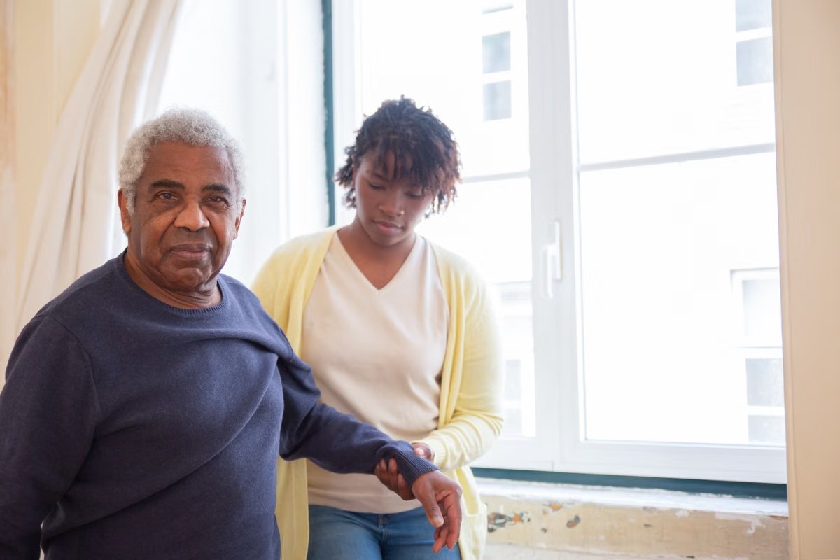 A caregiver steadying a senior man as he moves through his home